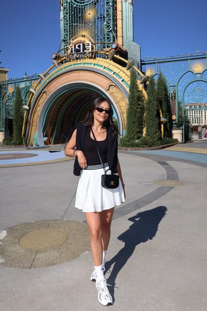 Black Tank Top + Black Sweater Draped Over Shoulders + White Pleated Mini Skirt + White Crew Socks + White Sneakers