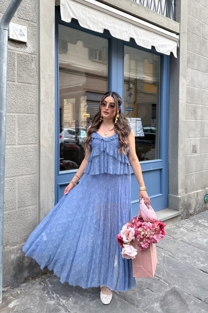 Blue Ruffled Tiered Maxi Dress + Gold Statement Earrings + Cat Eye Sunglasses + Pink Paper Gift Bag with Flowers + White Lace Flat Shoes