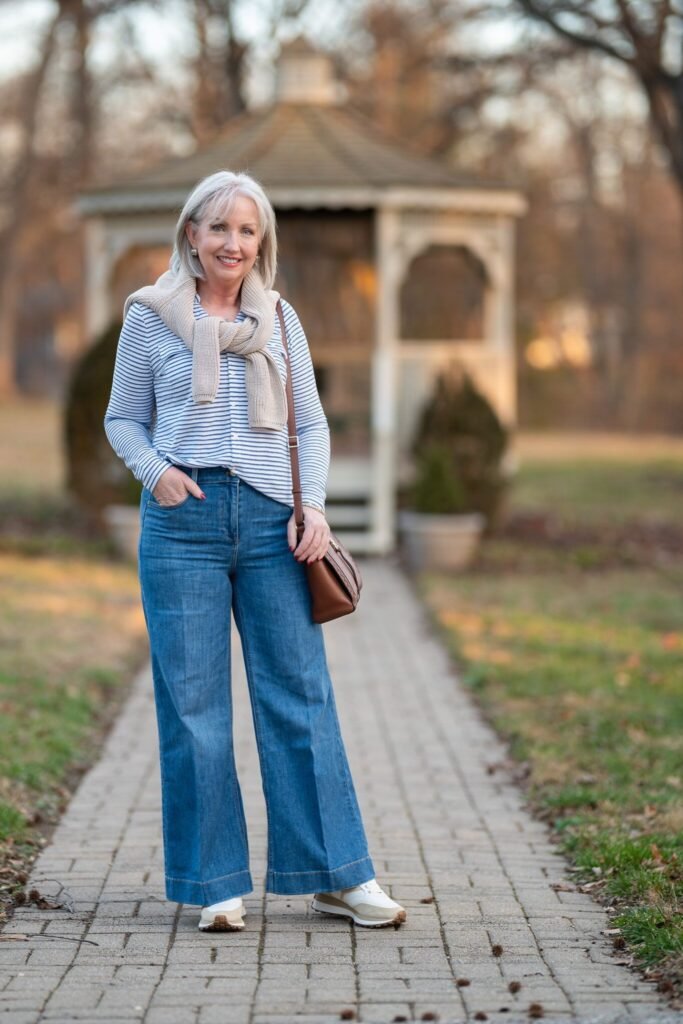 Blue and White Striped Button Down Shirt + Beige Knit Sweater (tied over shoulders) + Blue Wide Leg Jeans + White and Beige Sneakers