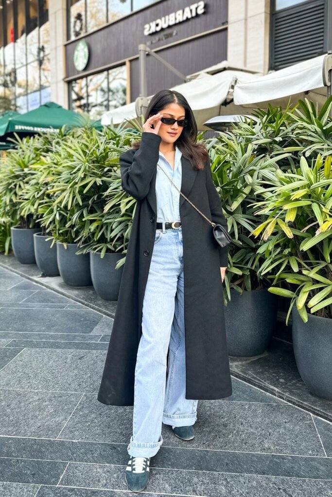 Long Black Coat + Light Blue Button Up Shirt + Light Wash Wide Leg Jeans + Dark Green Sneakers
