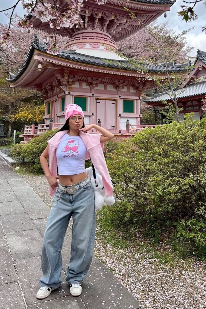 Pink Beanie + Hello Kitty Graphic Crop Top + Pink Sweater Slung Over Shoulders + Baggy Low Rise Light Wash Jeans